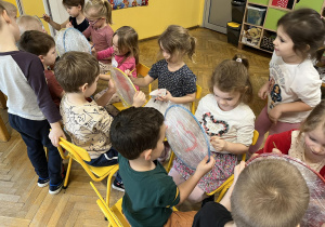 Na zdjęciu dzieci z grupy fioletowej siedzą na krzesełkach na wprost siebie i malują kółeczka oblepione folią