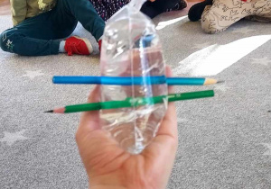 Na zdjęciu dzieci obserwują torebkę pełną wody przebitą przez dwa ołówki