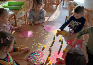 Na zdjęciu dzieci siedzą przy stole i ozdabiają serca wykonane z papieru