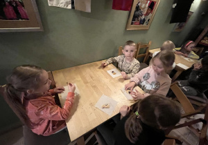 Na zdjęciu chłopcy i dziewczynki z grupy fioletowej siedzący przy stoliku w teatrze Baśniowa Kawiarenka, dzieci częstują się poczęstunkiem