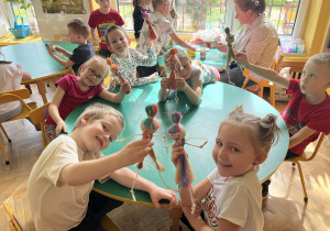 Na zdjęciu dzieci z grupy fioletowej podczas wykonywania laleczki ze sznurka, dzieci prezentują wykonane laleczki