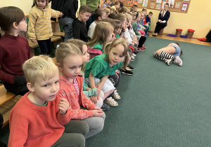 Na zdjęciu dzieci z grupy fioletowej podczas wycieczki do Szkoły Muzycznej dzieci siedzą na ławce i oglądają przedstawienie