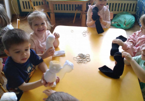 Na zdjęciu dzieci z grupy żółtej podczas warsztatów plastycznych, dzieci siedzą przy stole i wykonują kota ze skarpety