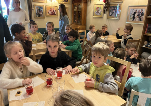 Na zdjęciu dzieci z grupy czerwonej podczas wycieczki do Baśniowej Kawiarenki, dzieci siedzą przy stole i częstują się poczęstunkiem