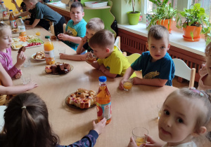 Na zdjęciu dzieci podczas jedzenie przysmaków z pikniku, dzieci siedzą przy stole i wspólnie spędzają czas