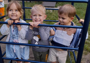 Na zdjęciu troje dzieci przy drabinkach, dzieci się uśmiechają.