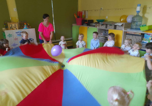 Dzieci stoją trzymając w rękach kolorową chustę animacyjną, za pomocą której podrzucają balona.