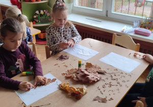 Na zdjęciu dzieci siedzące przy stoliku i wykonujące prace z liści