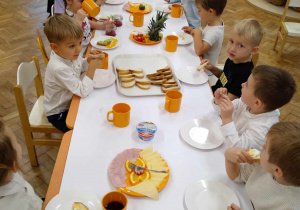 Na zdjęciu dzieci siedzące przy złączonych stołach, dzieci wspólnie zjadają posiłek