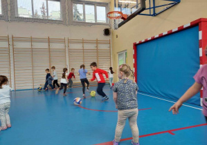 Na zdjęciu dzieci biegające i bawiące się piłkami w sali gimnastycznej