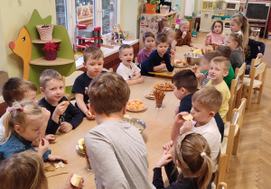 Dzieci z grupy zielonej podczas spotkania noworocznego, dzieci wspólnie jedzą słodkości przy stolikach