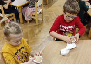 Na zdjęciu dzieci siedzące przy stoliku wykonują koty ze skarpety