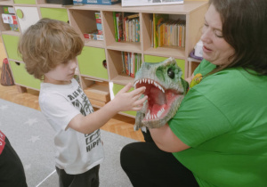 Na zdjęciu chłopiec z grupy pomarańczowej wkłada rączkę do paszczy dinozaura