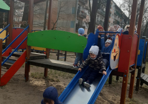Dzieci zjeżdżają na zjeżdżalni w kolorach czerwonym, zielonym i niebieskim.