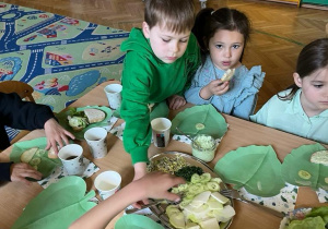 Na zdjęciu dzieci z grupy czerwonej przberane w ubrania o kolorze zielonym jedzą wspólnie śniadanie