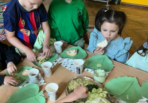 Na zdjęciu dzieci z grupy czerwonej przberane w ubrania o kolorze zielonym jedzą wspólnie śniadanie