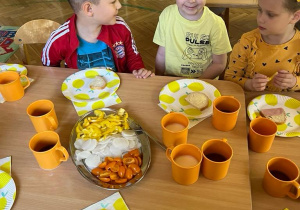 Na zdjęciu trójka dzieci z grupy czerwonej siedzi przy stoliku na śniadaniu dzieci są ubrane na żółto