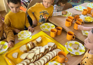 Na zdjęciu dzieci z grupy czerwonej siedzi przy stoliku na śniadaniu dzieci są ubrane na żółto
