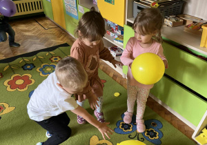 Na zdjęciu troje maluchów bawiących się żółtymi balonami