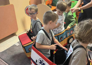 Na zdjęciach dzieci z grupy czerwonej podczas zajęć ze Strażą Miejską dzieci jeżdżą w samochodzikach nakładanych na dzieci, poruszają się za pomocą nóg