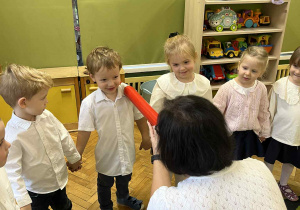 Na zdjęciu dyrekcja przedszkola pasująca przedszkolaki ubrane na galowo czerwoną kredką