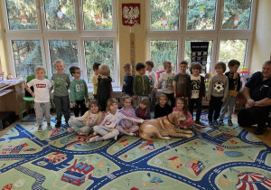 Na zdjęciu dzieci z grupy czerwonej pozyją do zdjecia z psem labradorem i funkcjonariuszem Straży Miejskiej