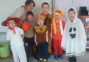 Na zdjęciu dzieci z grupy fioletowej dzieci stoją wraz z nauczycielem, dzieci są przebrane w kostiumy jesienne