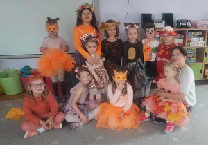 Na zdjęciu dzieci z grupy fioletowej dzieci stoją wraz z nauczycielem, dzieci są przebrane w kostiumy jesienne