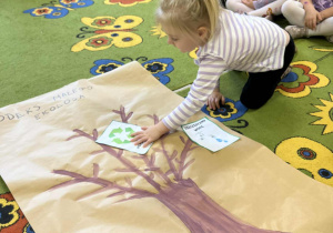 Na zdjęciu dziewczynka przyklejająca obrazek ekologiczny do namalowanego drzewa