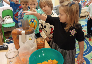 Na zdjęciu dziewczynka dokładająca owoce do sokowirówki