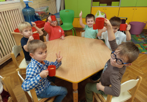 Na zdjęciu dzieci siedzące przy stole dzieci piją wykonany samodzielnie soczek