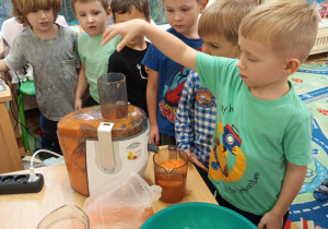 Na zdjęciu chłopiec dokładający owoce do sokowirówki