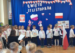 Na zdjęciu dzieci z grupy czerwonej, dzieci ubrane na galowo jeden z chłopców trzyma flagę, drugi mapę Polski