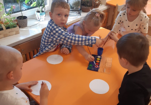 Dwie dziewczynki i trzech chłopców malują farbami na białym, papierowym talerzyku.