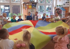 Dzieci ustawione są w kole, w rękach trzymają kolorową chustę animacyjną. Dzieci poruszają chustą w górę i w dół.