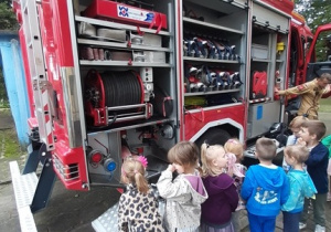 Dzieci stoją przy wozie strażackim. Oglądają jego wyposażenie.