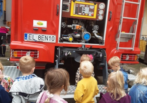 Dzieci stoją w gromadce, przyglądają się wyposażeniu wozu strażackiego.