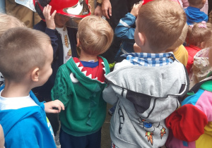 Dzieci stoją w luźnej gromadce. Dwóch chłopców przymierza hełmy strażakie.