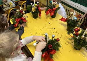 Na zdjęciu dzieci siedzące przy stole dzieci wykonują stroik świąteczny