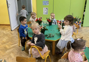 Na zdjęciu dzieci siedzące przy stołach dzieci wykonują stroik świąteczny