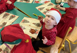 Na zdjęciu dzieci ubrane na czerwono w czapki mikołajowe ozdabiają pierniki
