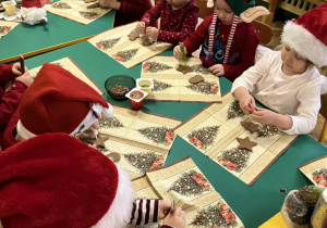 Na zdjęciu dzieci ubrane na czerwono w czapki mikołajowe ozdabiają pierniki