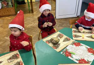 Na zdjęciu dzieci ubrane na czerwono w czapki mikołajowe ozdabiają pierniki