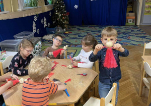 Na zdjęciu dzieci siedzą przy stołach i wykonują Mikołaja ze sznurka