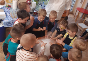 Chłopcy ustawieni wokół pomarańczowego stolika dotykają piany utworzonej z wody, suchego lodu i płynu do naczyń.