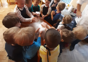 Chłopcy ustawieni wokół pomarańczowego stolika dotykają piany utworzonej z wody, suchego lodu i płynu do naczyń.