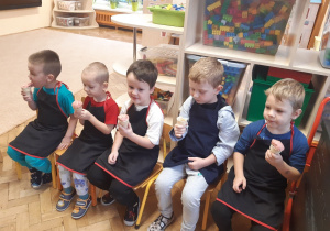 Pięciu chłopców siedzi na krzesełkach i je lody. W tle widać szafkę, na której stoją kolorowe klocki w przezroczystych pudełkach.