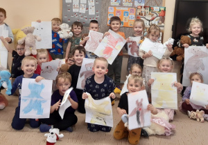 Dzieci pozują do zdjęcia trzymając w rękach swoje pluszowe misie i portrety swoich zabawek.