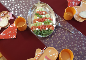 Na czerwonym obrusie położony jest biały bieżnik w srebrne gwiazdy. Na półmisku widoczne są warzywa i sery ułożone w kształt świątecznej choinki.