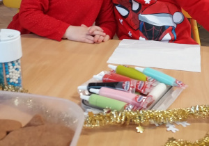 Na zdjęciu dzieci ozdabiające pierniki, chłopczyk ma mikołajową czapkę na głowie